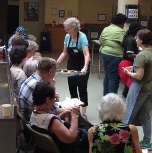 Food samples are handed out as part of a local outreach done in cooperation with a local garden project and a community cooking school. A dietitian speaks for the first half of the presentation, and then a chef demos healthy recipes.